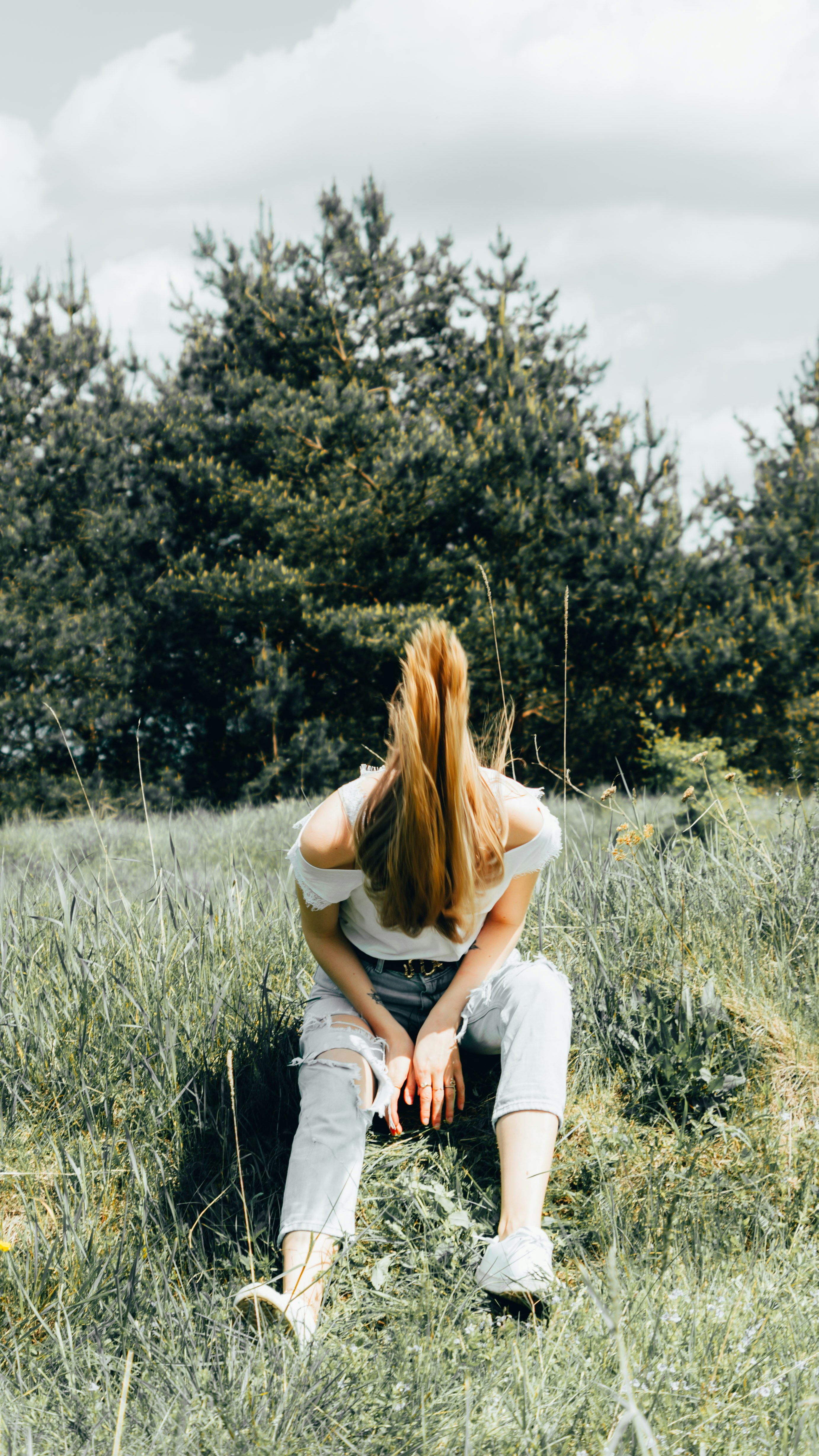 woman in white tank top sitting on green grass field during daytime